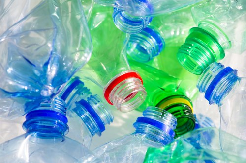 A close-up image displaying multiple discarded plastic bottles with various coloured caps, including green, blue, red, and black, arranged haphazardly on a reflective surface. The bottles are translucent and appear crumpled and empty, indicating they are used. The background reveals additional plastic bottles, suggesting a larger collection of waste. This scene depicts typical plastic rubbish collected during garden or household clearance services, such as those offered by Garden Clearance Palmers Green, serving clients in the local area. The distribution of bottles and caps highlights the common types of plastic waste that require proper disposal or recycling, relevant to rubbish removal and waste management operations in the vicinity of Palmers Green, N13. The lighting is bright, emphasizing the transparency and vibrant colours of the plastic debris, creating a clear visual context of plastic waste accumulation that professional rubbish removal services aim to address for local residents.